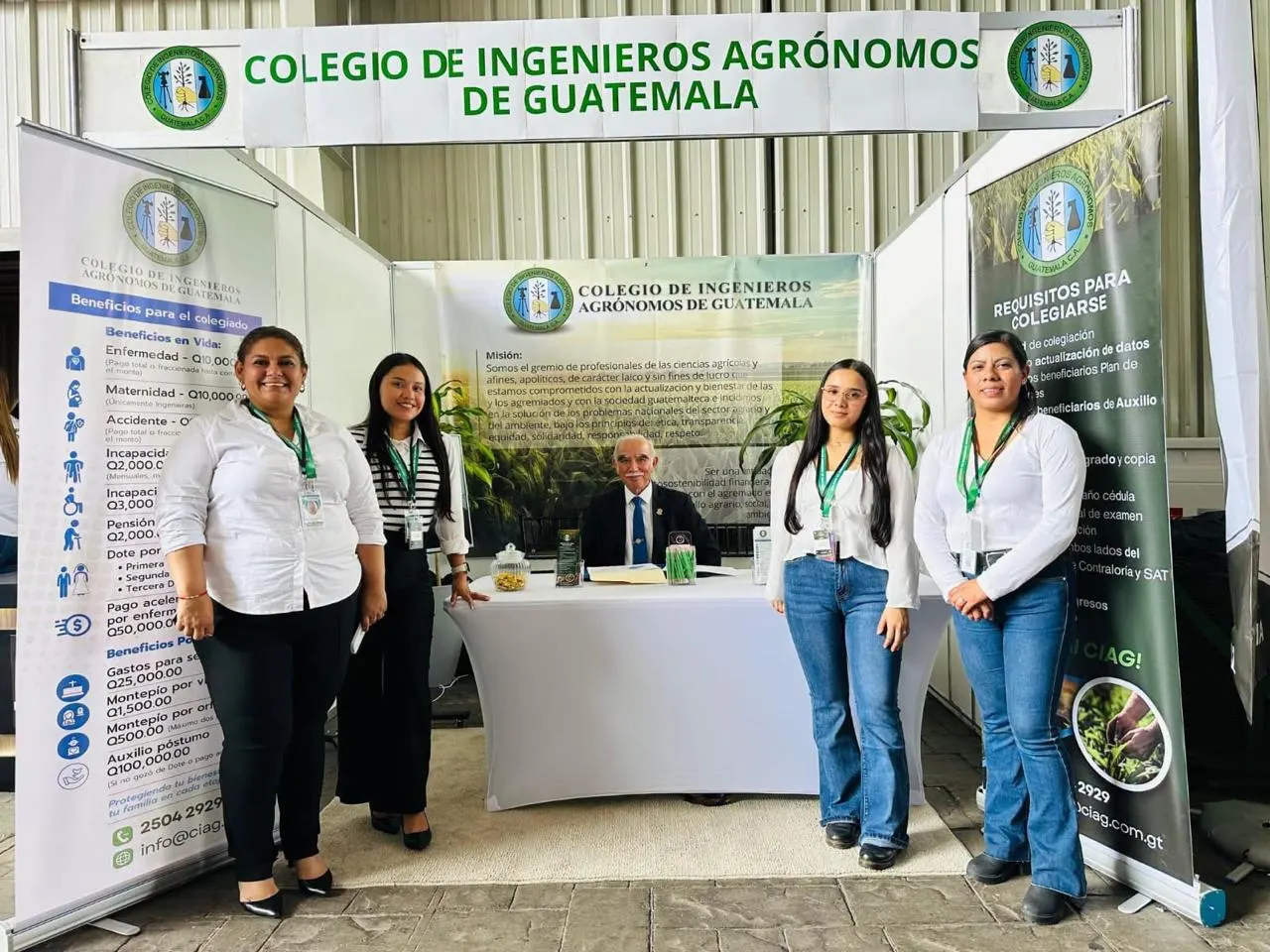 Representantes del CIAG en un evento institucional ante el distintivo del Colegio